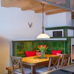 Ferienwohnung Innenräume: Kachelofen mit Altholz-Esstisch und rustikaler Ofenbank sowie schönen Stühlen